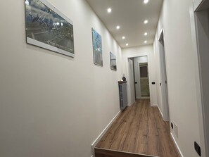 A hallway with wooden flooring, white walls, and recessed ceiling lights.