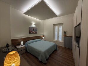 A bedroom with a bed, bedside tables, a nightstand, a window, and a ceiling light fixture. - Relais Pietro Luxury Apartment (Barzago)