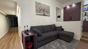Una sala de estar moderna con un sofá seccional gris, una mesita con piezas de ajedrez, un cuadro de flores y una escalera que conduce a otra habitación.