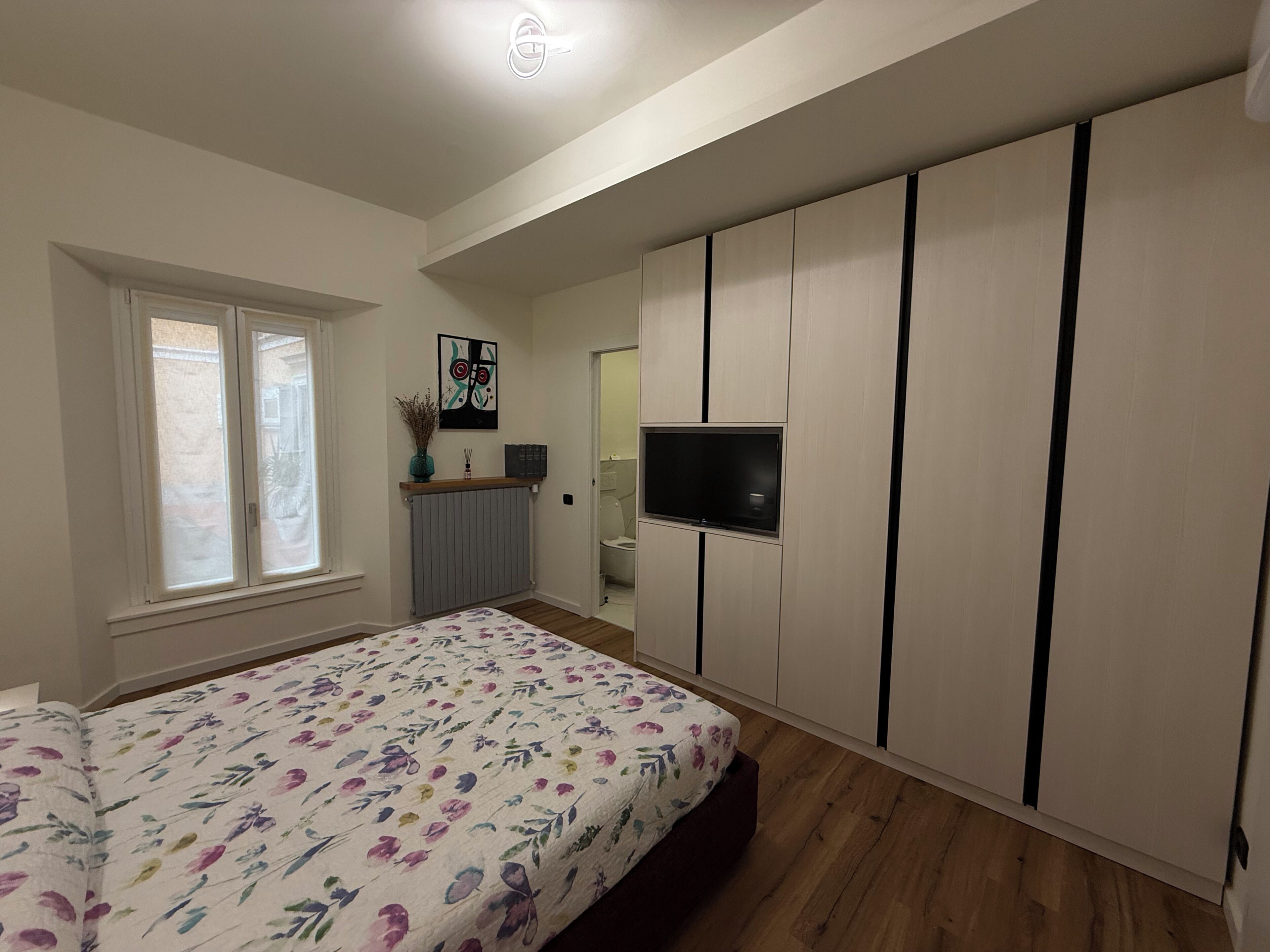 Un dormitorio con cama, televisión, radiador y ventana.