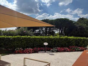 An outdoor seating area with a table and chairs, a large umbrella, and a hedge with red and white flowers. - Relais Pietro Luxury Apartment (Barzago)