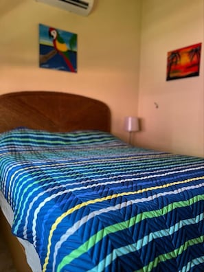 A bed with a blue and green striped bedspread, a wooden headboard, and two paintings on the wall. - Poolside 2-Bedroom Retreat | Walking Distance to Coco Beach (Guanacaste Province)