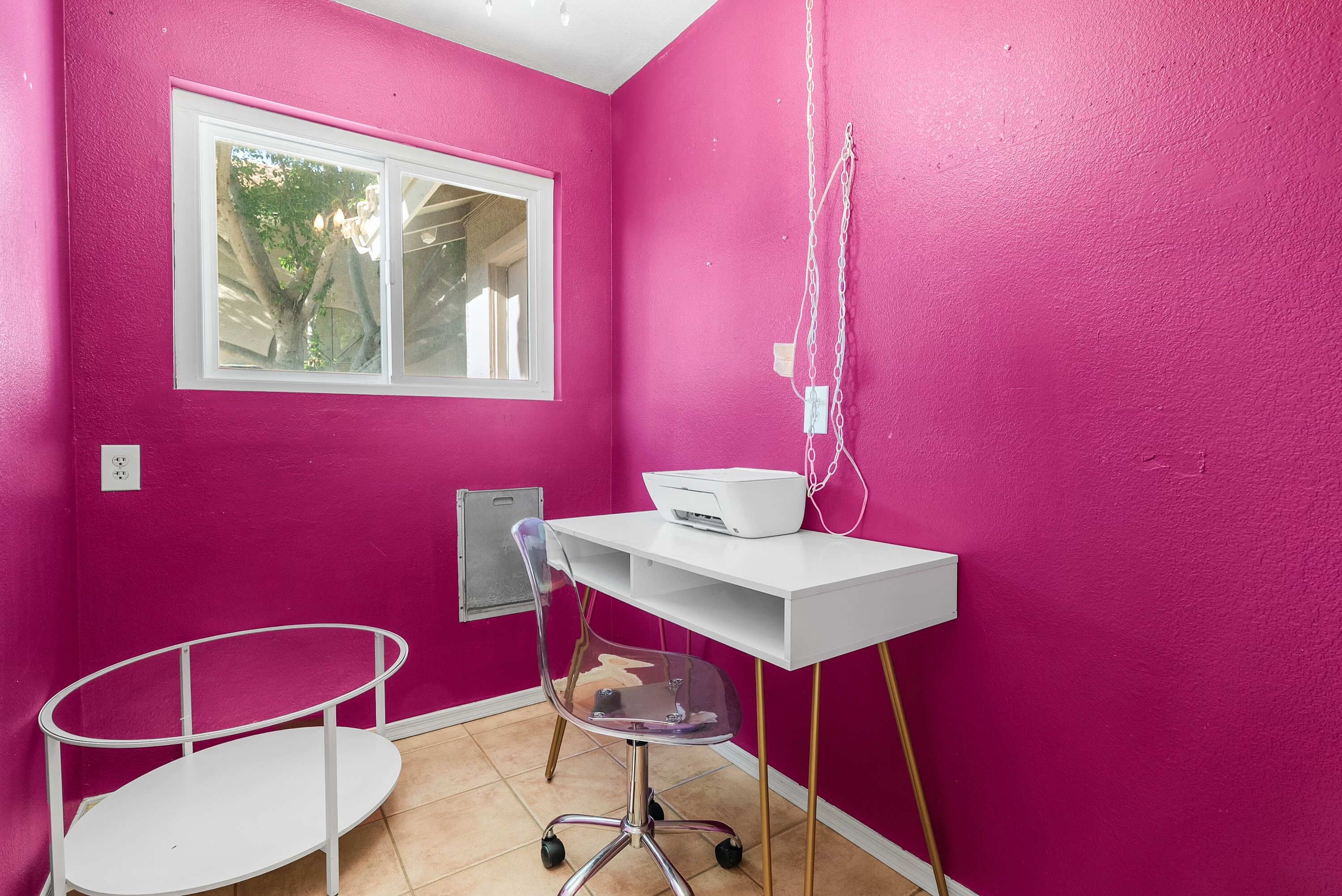 A room with pink walls, a white desk, a chair, and a window.