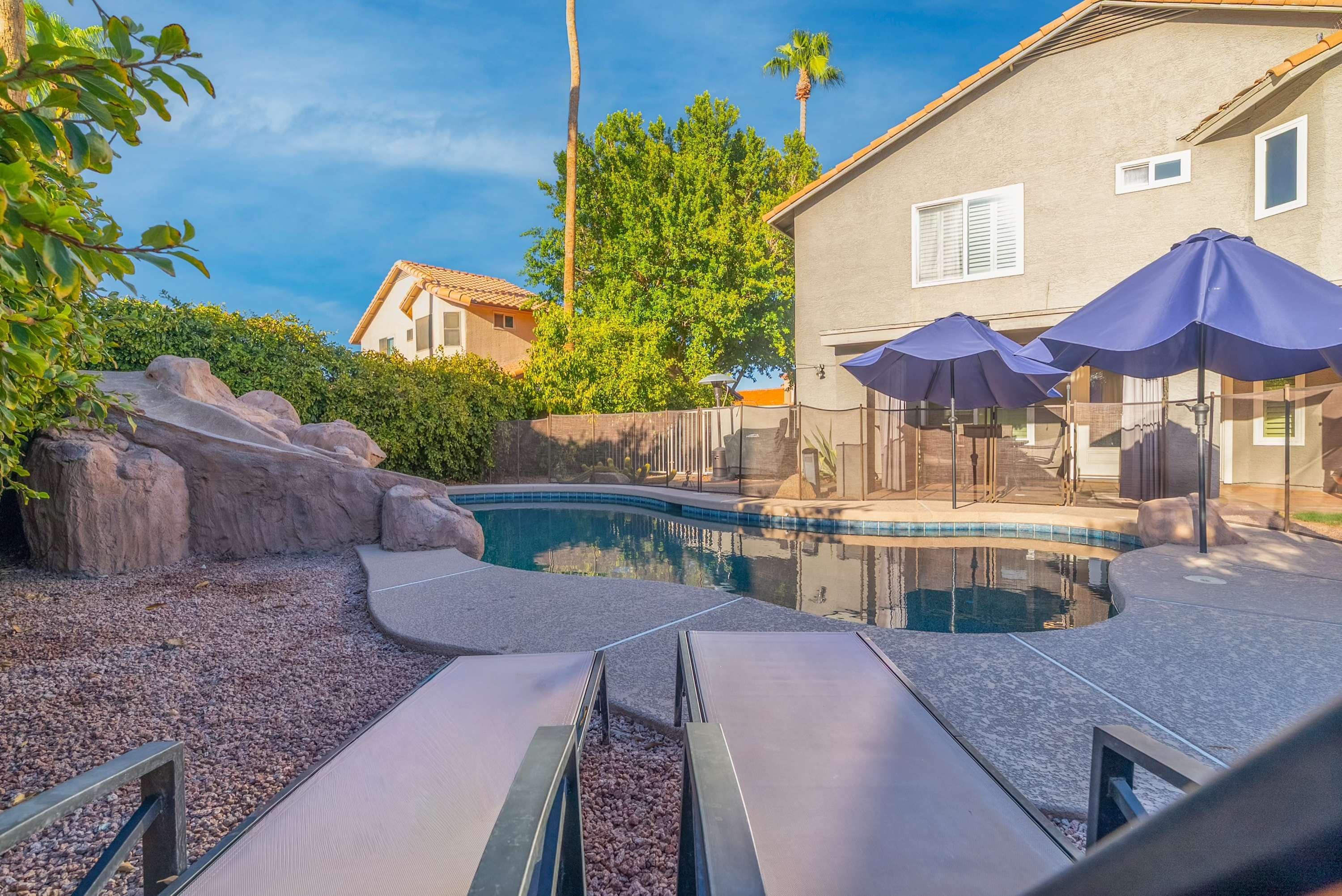 A swimming pool with lounge chairs and umbrellas, surrounded by rocks and greenery.