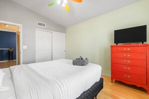 Ein Schlafzimmer mit einem Bett, einer roten Kommode, einem Fernseher und einem Deckenventilator.