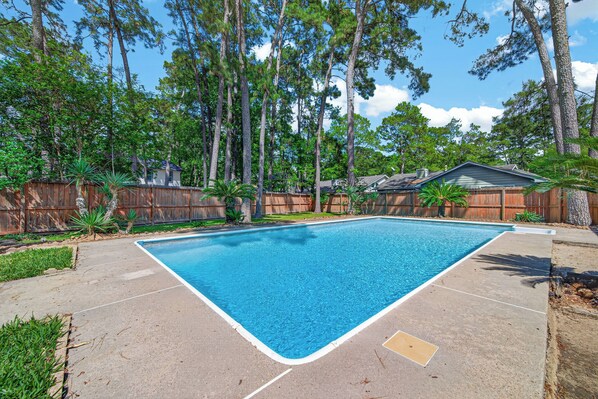 Une piscine rectangulaire à l’eau d’un bleu limpide, entourée d’une terrasse en béton et d’une clôture en bois.