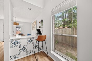 A kitchen with a white countertop, patterned backsplash, and a window overlooking a wooden fence and greenery.