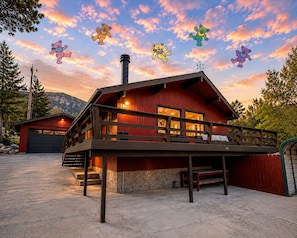 A red cabin with a balcony, a garage, and a mountain backdrop. - Sunshine Daydream /Town Center/RV Parking/AC/River (Kernville)