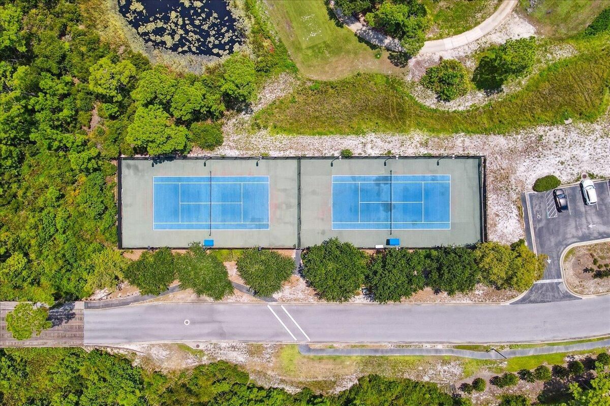 An aerial view of a tennis court facility with two courts, surrounded by greenery and adjacent to a road.
