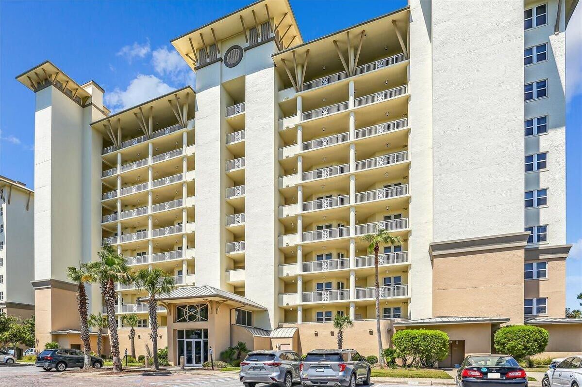 A multi-story hotel with balconies, a central entrance, and palm trees.