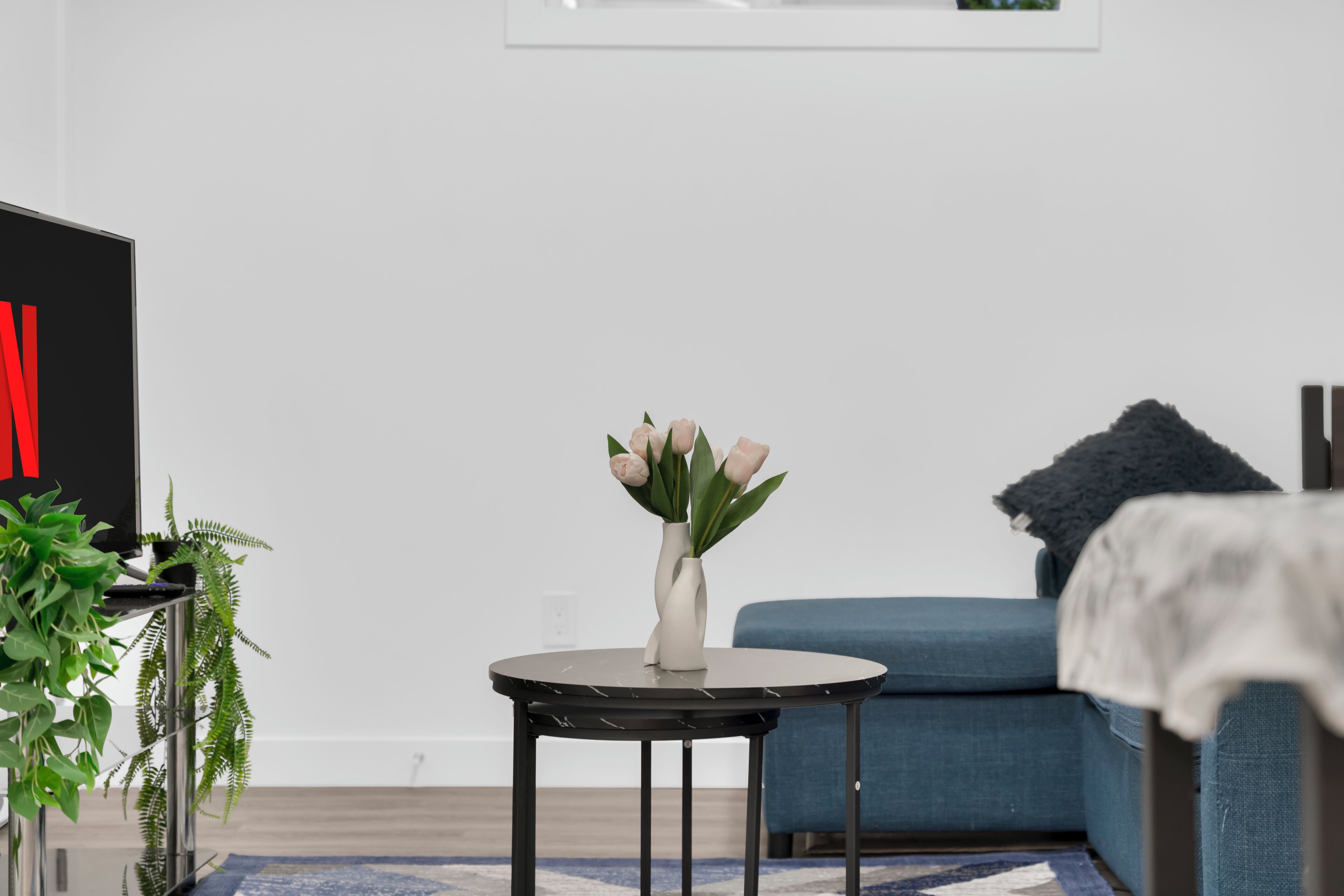 Un salon moderne avec une table ronde, un canapé bleu et un vase rempli de fleurs.