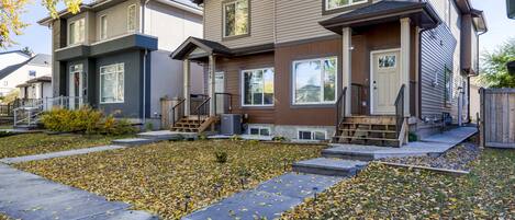 A row of townhouses with a front yard, a wooden deck, and a clear sky.