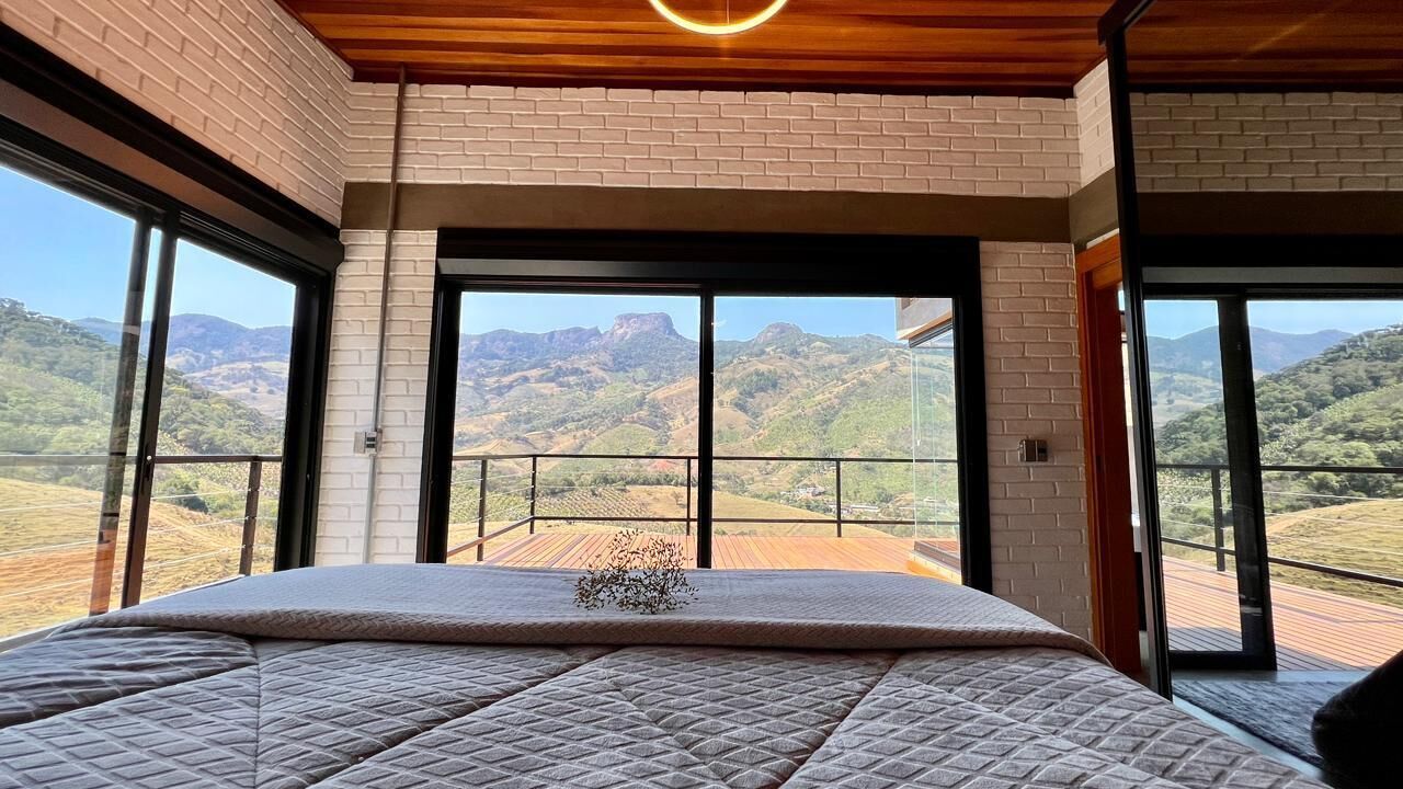 Een slaapkamer met een groot bed, uitzicht op het platteland via een balkon en een houten plafond.