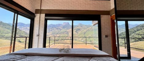 Un dormitorio con una cama grande, vista al campo desde un balcón y techo de madera.