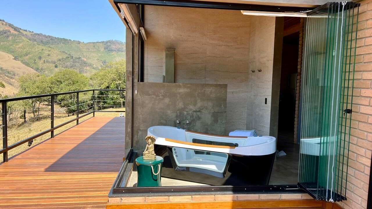A modern bathroom with a bathtub and a shower, a wooden deck, and a view of the hills.
