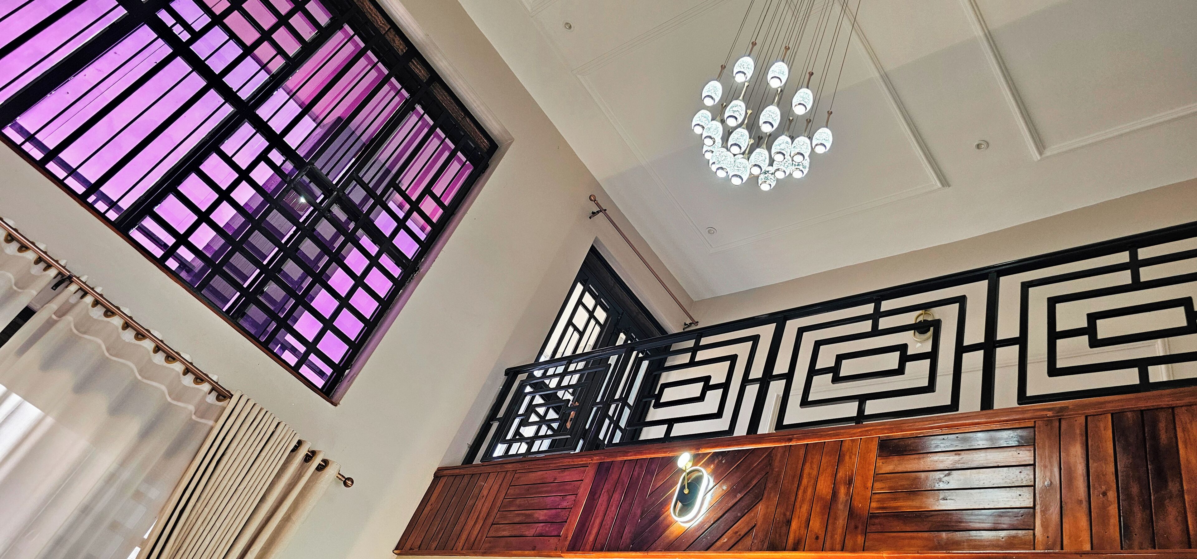 Une pièce avec un plafond en bois, un luminaire décoratif et une fenêtre ornée d’un motif quadrillé aux nuances violettes.