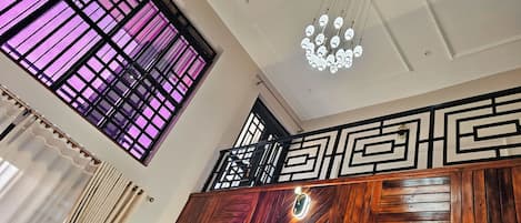 A room with a wooden ceiling, a decorative light fixture, and a window with a purple-tinted grid pattern.