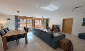 A modern living room with a dining area, a sofa set, a television, and a wooden table. - SPACIOUS 3-BEDROOM FAMILY APARTMENT WITH ALPINE VIEWS (Lauterbrunnen)