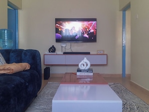 En stue med et fjernsyn ophængt på væggen, en sofa, et sofabord og en dekorativ genstand på bordet.