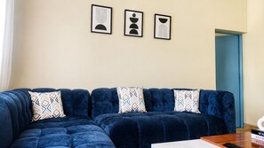 Un salon avec un canapé bleu, des coussins à motifs et trois œuvres d’art encadrées accrochées au mur.