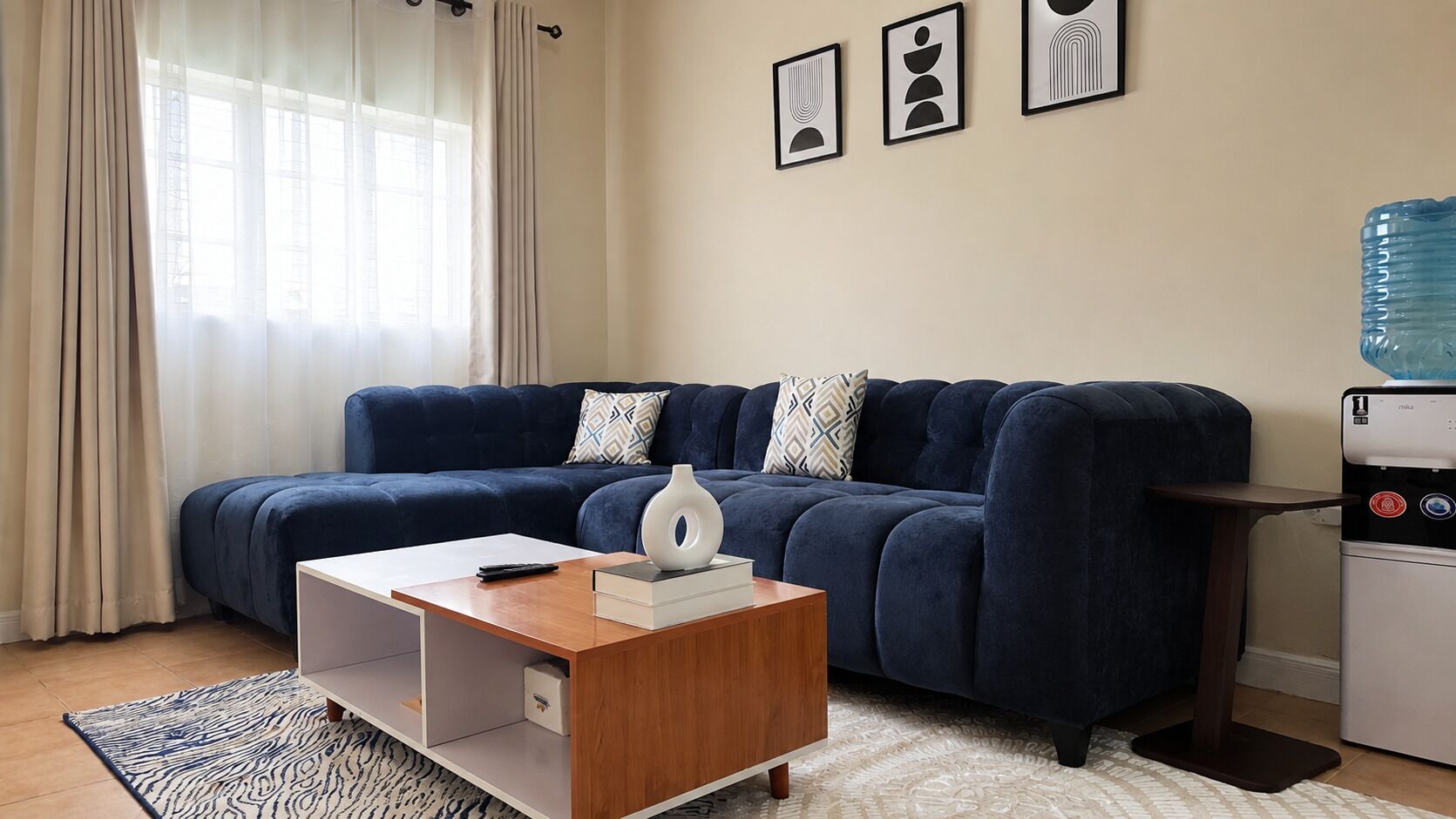Una sala moderna con un sofá azul oscuro, una mesa de centro de madera y un dispensador de agua.