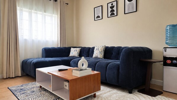 A modern living room with a dark blue sofa, a wooden coffee table, and a water dispenser.