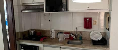 Una cocina compacta con microondas, lavaplatos y escurreplatos.