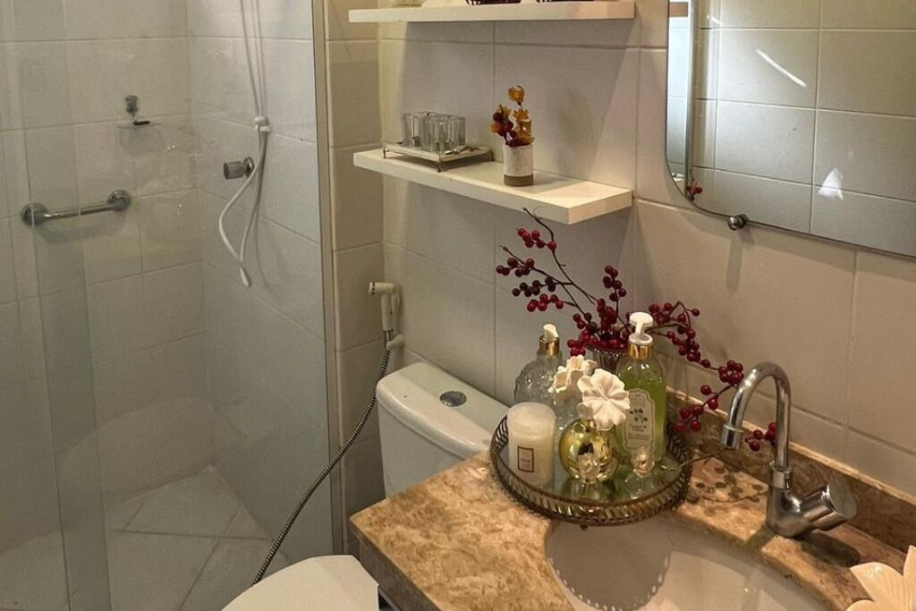 Ein Badezimmer mit Dusche, Toilette und Waschbecken. Über dem Waschbecken befinden sich Regale mit Pflegeprodukten und einer Dekovase.