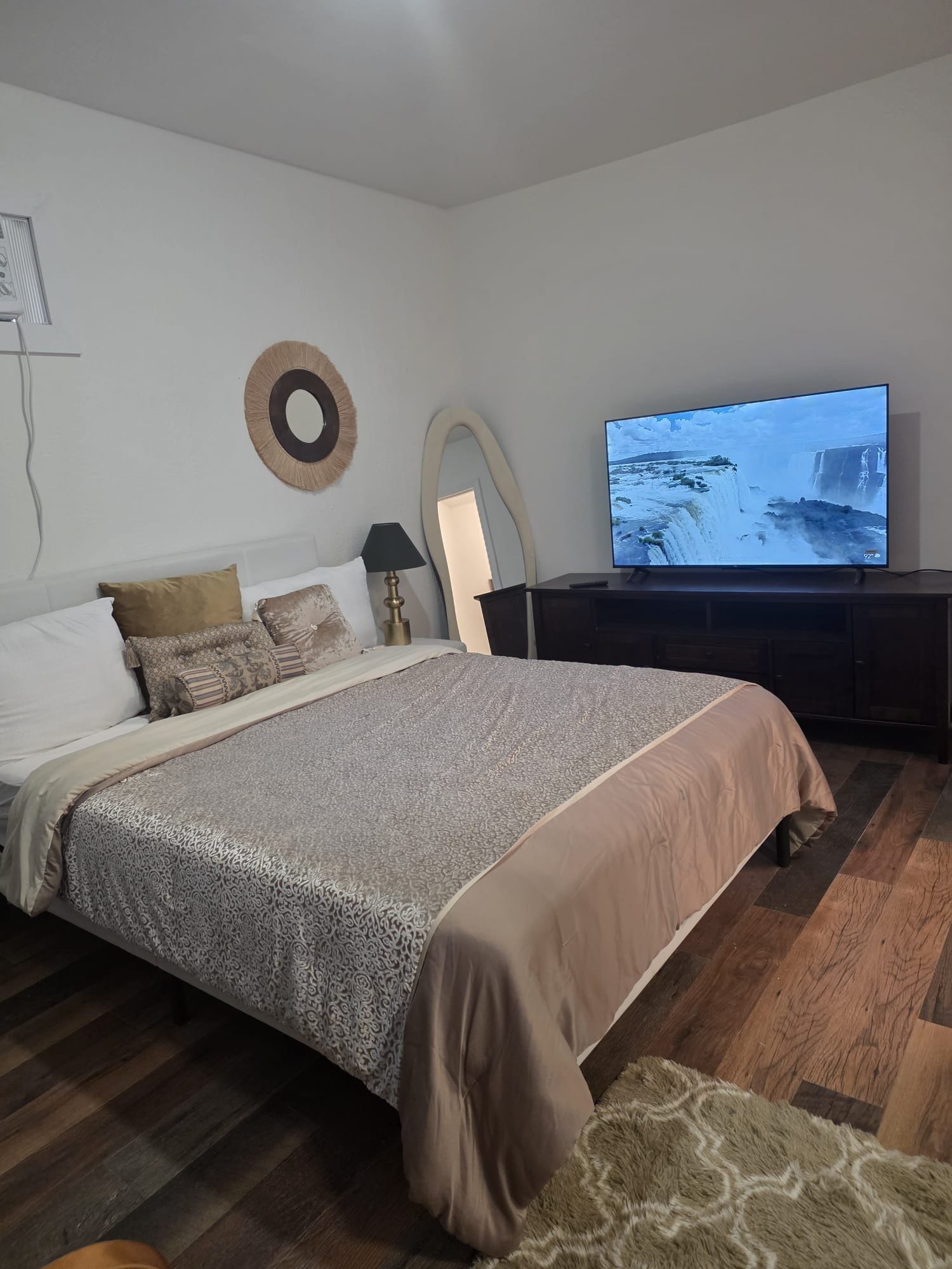 Un dormitorio con una cama grande, televisión y espejo montado en la pared.