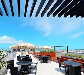 Eine Terrasse im Freien mit Tischen, Stühlen, Sonnenschirmen und Meerblick.