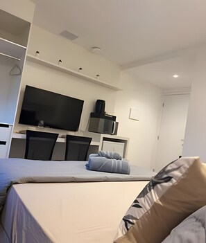 Ein modernes Hotelzimmer mit einem großen Bett, einem Flachbildfernseher, einem Schreibtisch mit Computer und einem Sessel.