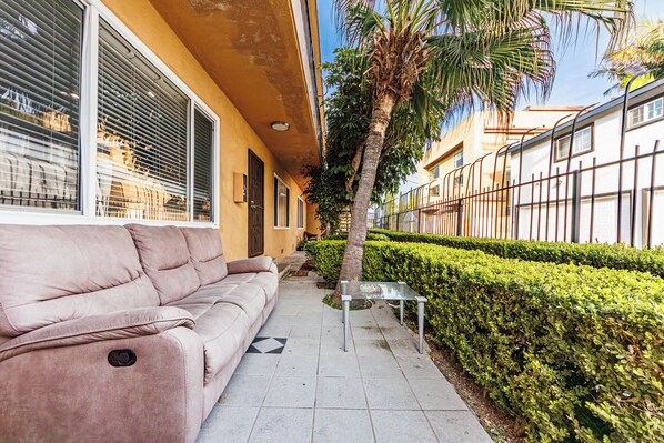 A beige sofa, a glass table, and a neatly trimmed hedge along a sidewalk. - Pretty apartment (Los Angeles)