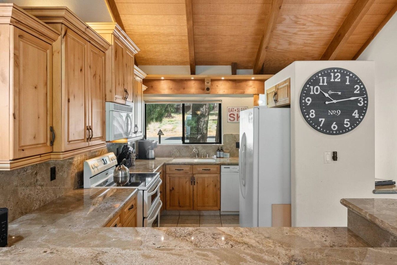 A kitchen with wooden cabinets, a stove, a sink, and a clock on the wall.