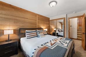 Ein Schlafzimmer mit einem hölzernen Kopfteil, einem Bett mit gemusterten Betttextilien, Nachttischlampen, einem Nachttisch und einem Spiegel.