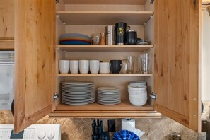 A kitchen cabinet with shelves holding plates, cups, and a coffee maker. - Indian Hills Townhome (Truckee)