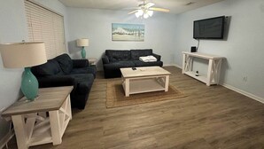 Un salon avec un canapé, une table basse, une lampe et un téléviseur fixé au mur.
