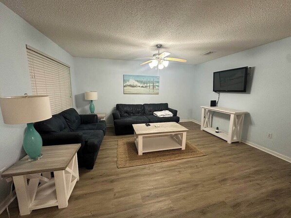 A living room with a sofa, coffee table, lamp, and a TV on the wall.
