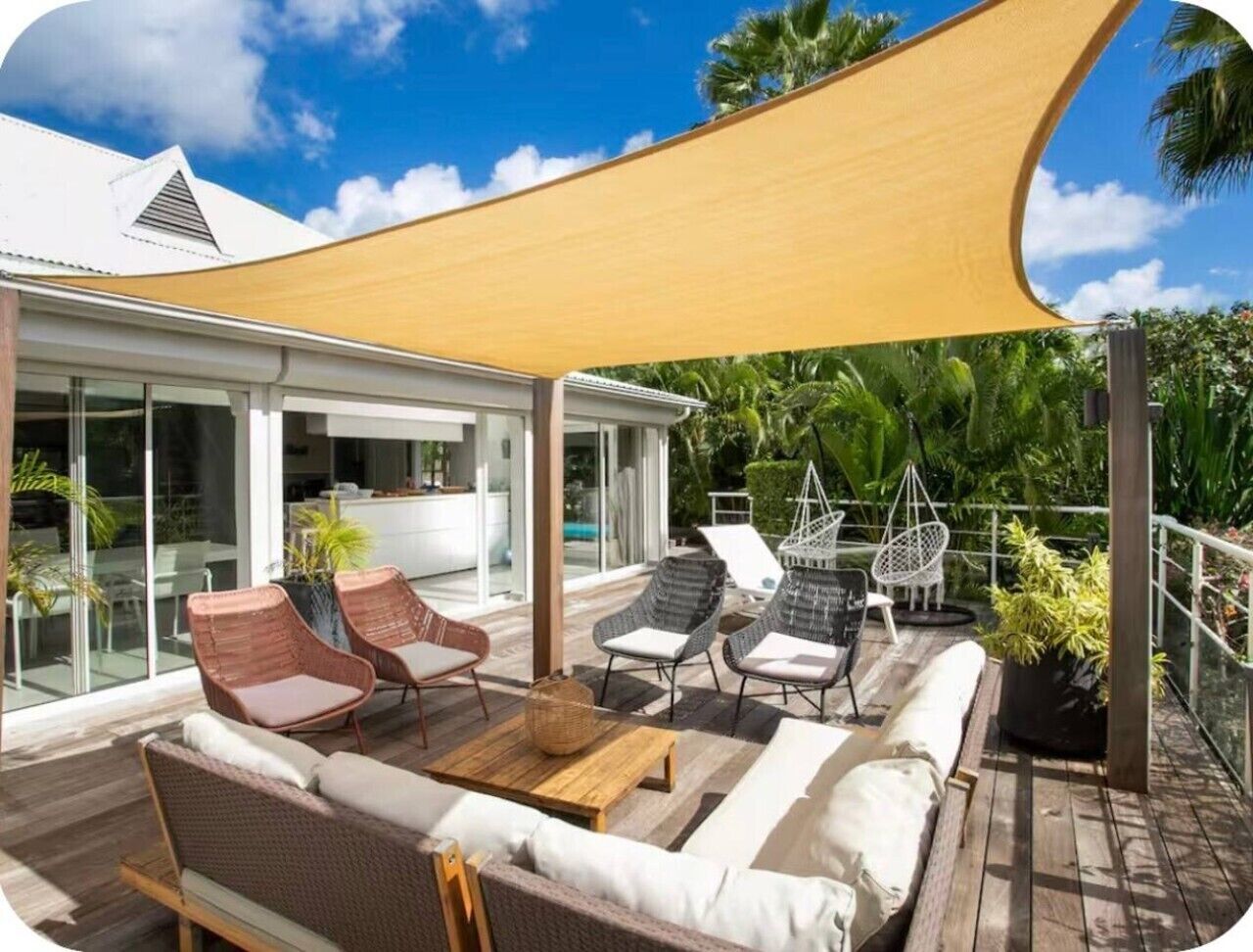 Un espace extérieur ensoleillé, aménagé avec des meubles en osier, une table en bois et une grande voile d’ombrage.