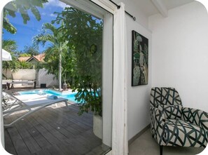A room with a pool, a chair, and a door leading to an outdoor area with trees and a view of a house. - Villa Elé, 4 bedrooms, tropical garden and pool (Orient Bay)