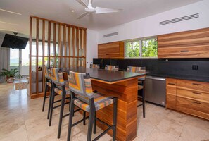 A modern kitchen with a central island, wooden cabinets, and a dining area with striped chairs. - Oceanview home in Mar Vista | 3 en-suite bedrooms  - Casa Cocobolo (Playa Flamingo)
