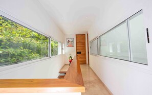 A modern hallway with large windows, a wooden bench, and a door with a wooden panel. - Oceanview home in Mar Vista | 3 en-suite bedrooms  - Casa Cocobolo (Playa Flamingo)