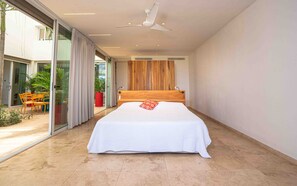 A modern bedroom with a large bed, a ceiling fan, and a sliding glass door leading to an outdoor area with plants and furniture. - Oceanview home in Mar Vista | 3 en-suite bedrooms  - Casa Cocobolo (Playa Flamingo)