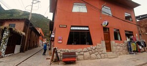 A two-story building with a massage parlor sign, a stone wall, and a clothing rack outside. - IMASMATI WASI (Pisac)