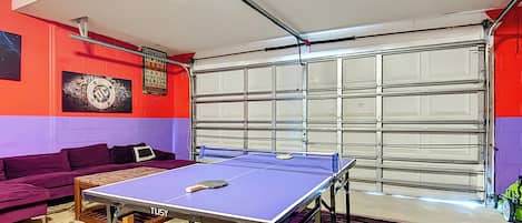 Una habitación con mesa de ping pong, un sofá púrpura, un tapete y una puerta de garaje.