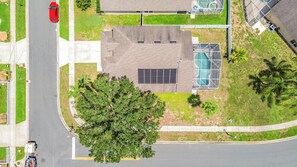 Eine Luftaufnahme eines Wohngebiets mit einem Haus, einem Swimmingpool, einem großen Baum und einem roten Auto, das auf der Straße geparkt ist.