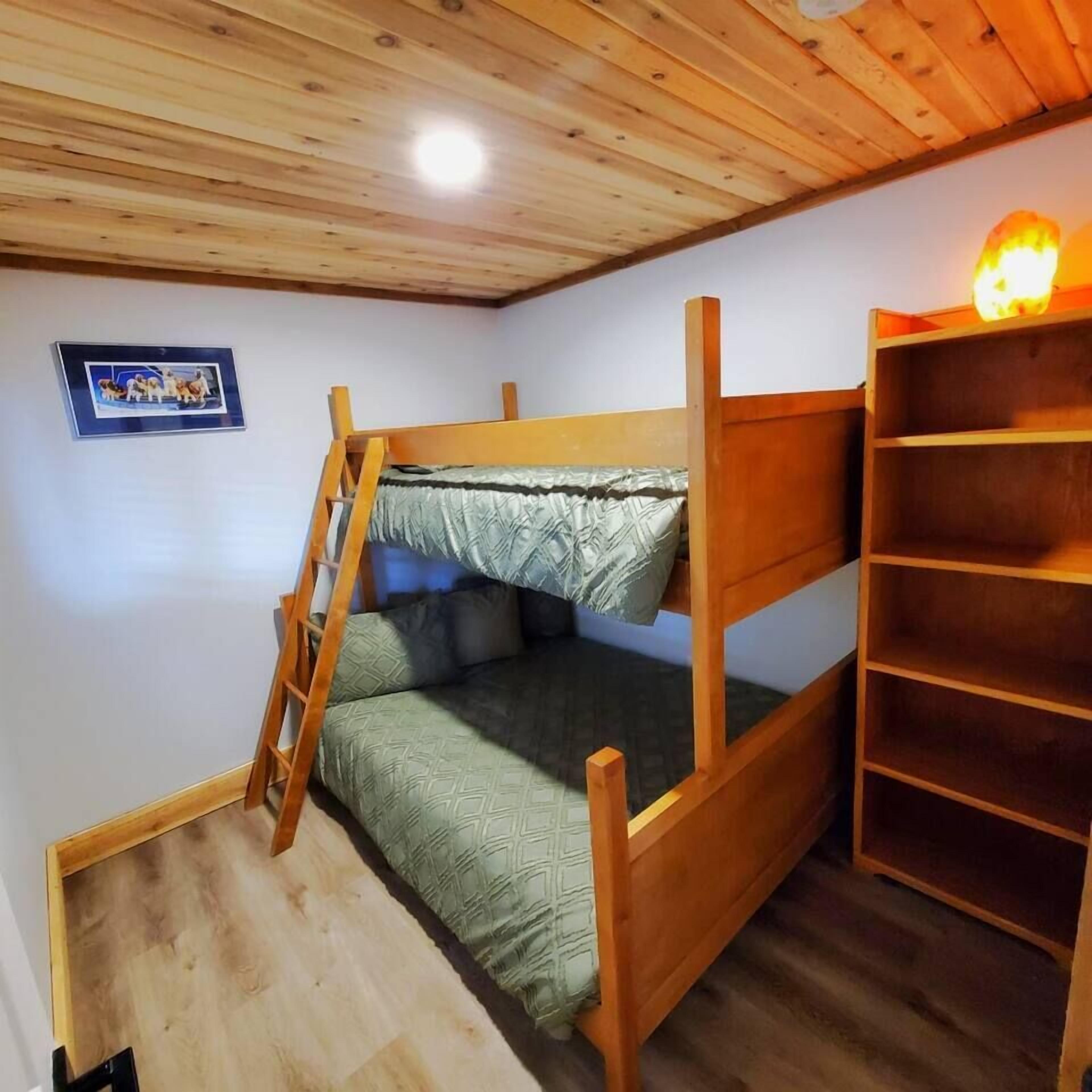 A bunk bed with a ladder, a shelf unit, and a framed picture on the wall.