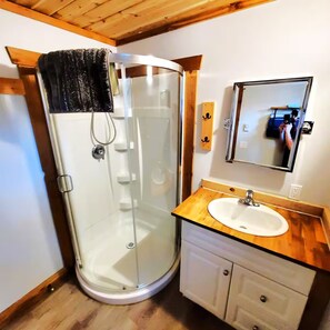 A bathroom with a glass shower enclosure, a wooden vanity with a sink, and a mirror above the vanity. - Tiny Home 10A | 2BDR (Terrace)