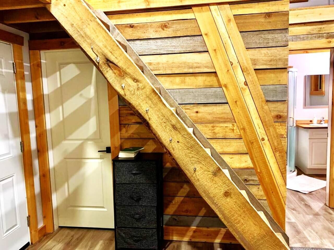 A wooden staircase in a room with a white door and a black cabinet.