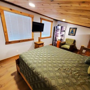 A bedroom with a bed, a television, a chair, and a bookshelf.