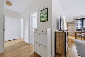 A modern interior with a wooden floor, white cabinetry, a desk with a computer, and a dining area with a table and chairs. - Warsaw Urban Wola Apt — Parking & Balcony (Warsaw)